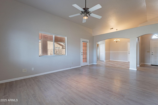 empty room featuring ceiling fan with notable chandelier, high vaulted ceiling, and light hardwood / wood-style floors