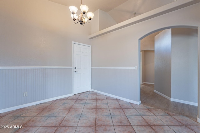 tiled spare room featuring lofted ceiling and a chandelier