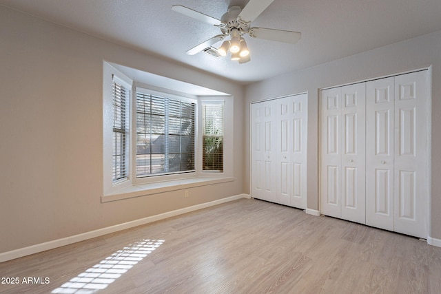 unfurnished bedroom with multiple closets, ceiling fan, and light wood-type flooring