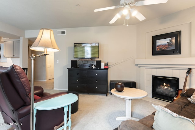 living room with a tile fireplace, light carpet, and ceiling fan