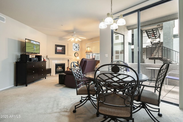 dining room featuring a tiled fireplace, light colored carpet, and ceiling fan with notable chandelier