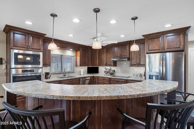 kitchen featuring a sink, under cabinet range hood, stainless steel appliances, a breakfast bar area, and decorative backsplash