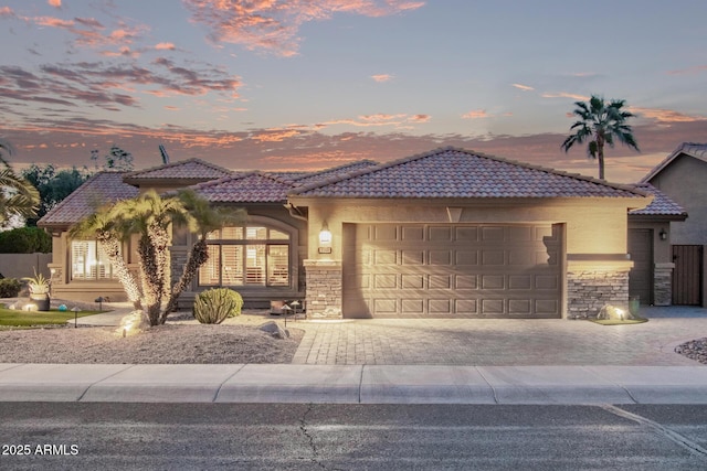 view of front of house featuring a garage, stone siding, a tile roof, and stucco siding