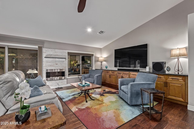 living area with vaulted ceiling, a stone fireplace, dark wood-type flooring, and visible vents