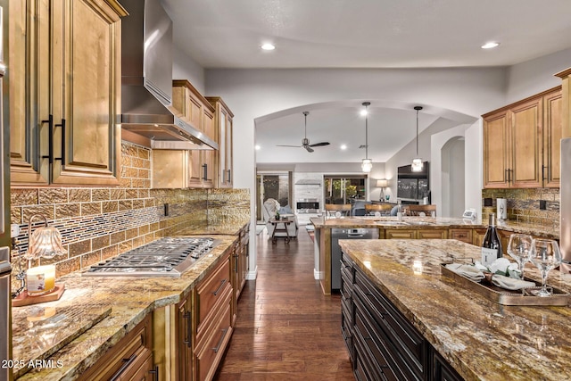 kitchen with arched walkways, ceiling fan, wall chimney exhaust hood, open floor plan, and stainless steel gas cooktop