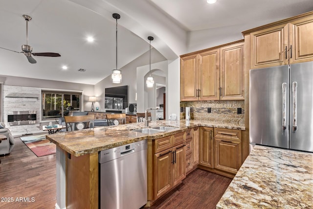 kitchen with light stone counters, appliances with stainless steel finishes, open floor plan, a sink, and vaulted ceiling