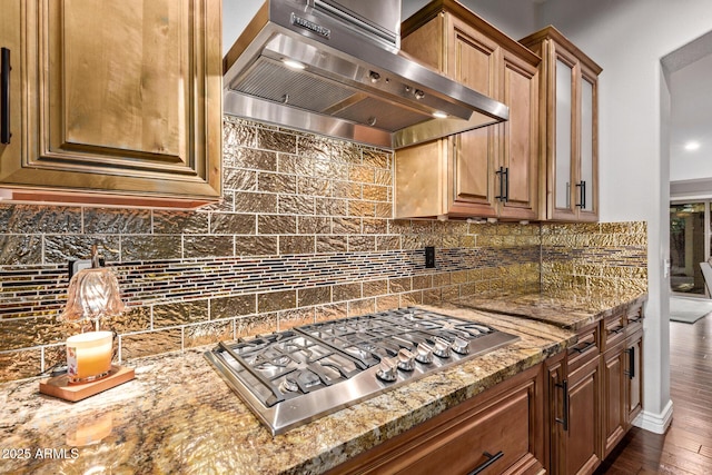 kitchen with tasteful backsplash, wall chimney range hood, light stone countertops, and stainless steel gas stovetop