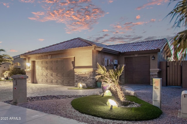 view of front facade featuring stone siding, a tiled roof, an attached garage, and driveway