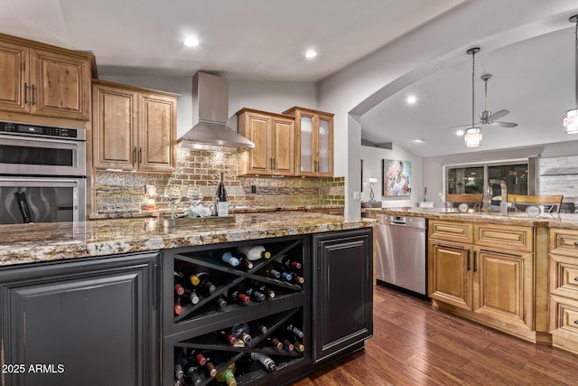 kitchen with lofted ceiling, arched walkways, stainless steel appliances, wall chimney exhaust hood, and dark wood finished floors