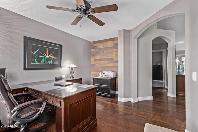 home office featuring baseboards, ceiling fan, arched walkways, and dark wood-style flooring