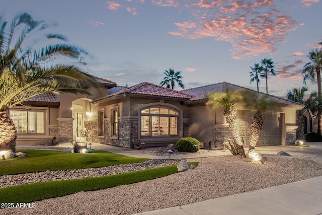 mediterranean / spanish house featuring stone siding, driveway, an attached garage, and stucco siding