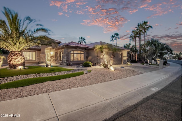 mediterranean / spanish-style home featuring a garage, concrete driveway, stone siding, a tiled roof, and stucco siding