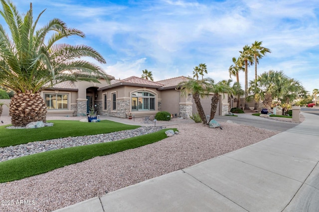 mediterranean / spanish home with stucco siding, an attached garage, stone siding, driveway, and a tiled roof