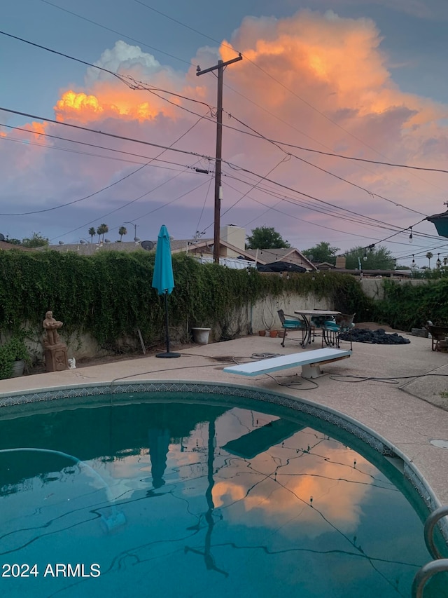 pool at dusk featuring a diving board and a patio area