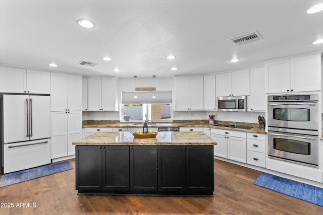 kitchen with stainless steel appliances, a center island, light stone counters, and dark wood-type flooring