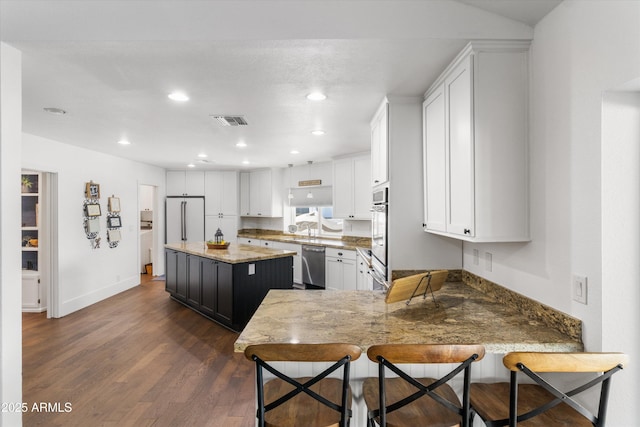 kitchen with stainless steel dishwasher, white cabinets, a kitchen island, dark hardwood / wood-style flooring, and light stone counters