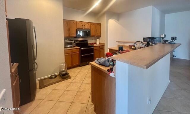 kitchen with kitchen peninsula, electric range, light tile patterned floors, and fridge