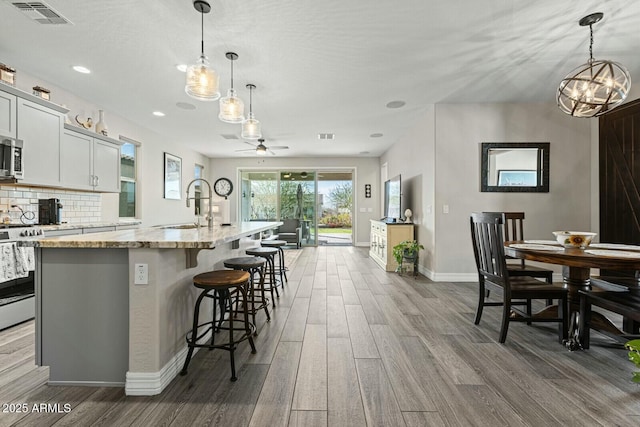 kitchen with pendant lighting, a breakfast bar area, light stone counters, stainless steel appliances, and a center island with sink