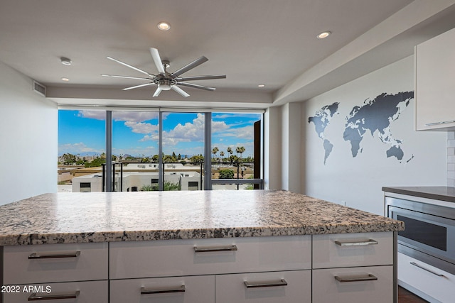 kitchen featuring ceiling fan, white cabinets, light stone countertops, and stainless steel microwave