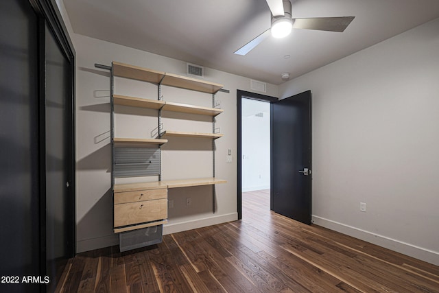 unfurnished bedroom with ceiling fan, a closet, built in desk, and dark wood-type flooring