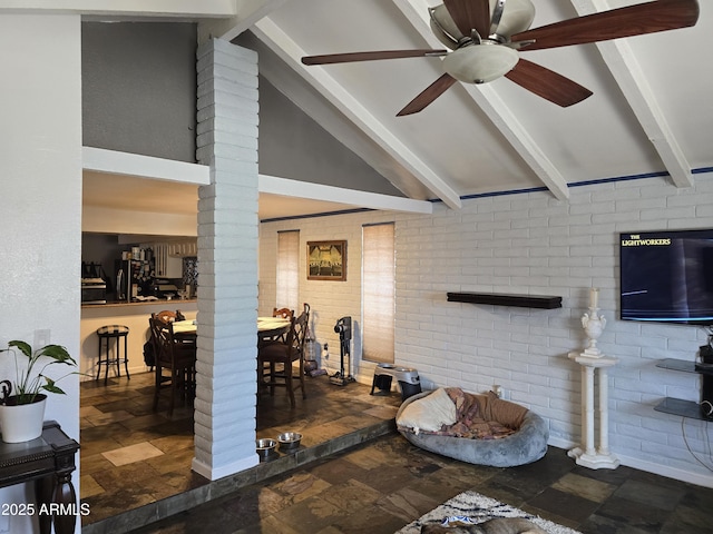 living room featuring a ceiling fan, lofted ceiling with beams, stone tile floors, brick wall, and decorative columns