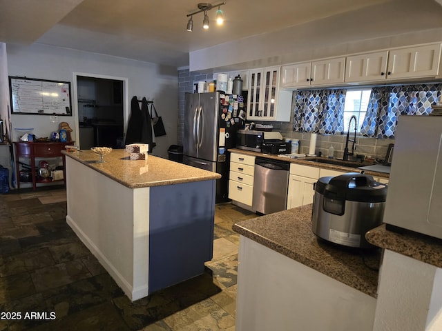 kitchen featuring decorative backsplash, a sink, white cabinetry, stainless steel appliances, and glass insert cabinets