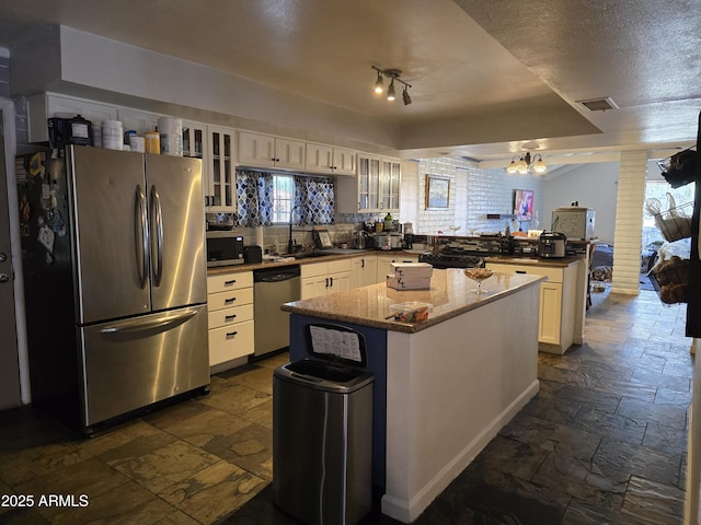 kitchen with visible vents, a sink, stone tile flooring, stainless steel appliances, and a peninsula