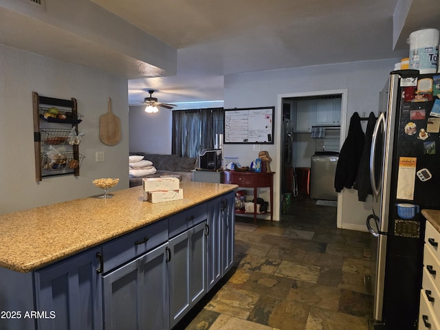kitchen featuring stone finish flooring, light stone countertops, washer / dryer, freestanding refrigerator, and a ceiling fan