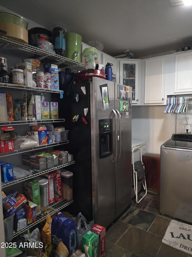 kitchen featuring stainless steel fridge with ice dispenser, white cabinets, stone finish floor, glass insert cabinets, and washer and dryer
