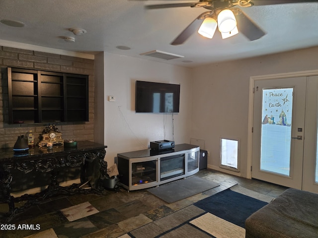 living room with stone tile flooring, visible vents, and a ceiling fan