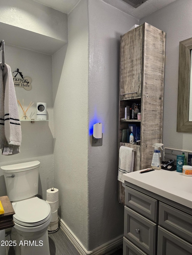 half bath featuring toilet, vanity, baseboards, and a textured wall