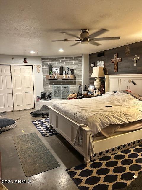 bedroom featuring ceiling fan, a fireplace, concrete flooring, and a textured ceiling