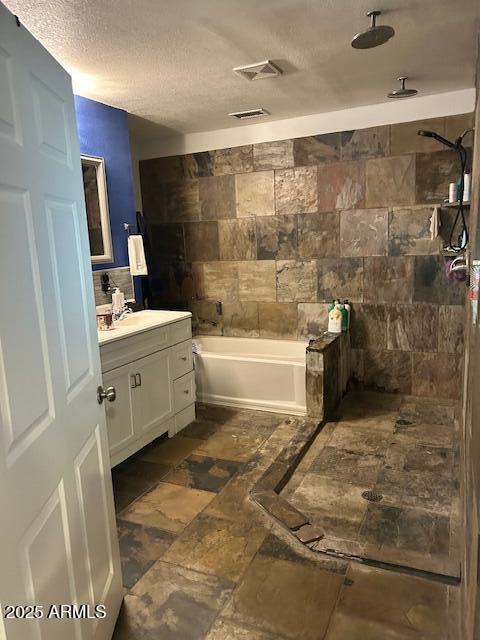 bathroom with visible vents, a washtub, a textured ceiling, tiled shower, and vanity