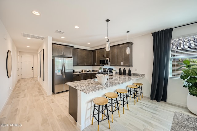 kitchen featuring appliances with stainless steel finishes, a kitchen bar, kitchen peninsula, light stone countertops, and dark brown cabinets