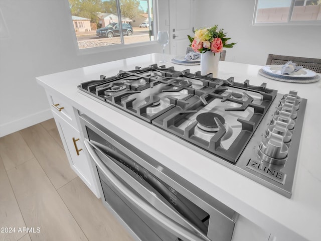 room details featuring appliances with stainless steel finishes, white cabinetry, and light hardwood / wood-style flooring