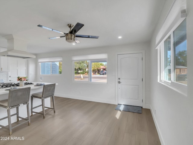 interior space featuring ceiling fan, white cabinetry, a kitchen bar, light hardwood / wood-style floors, and wall chimney exhaust hood