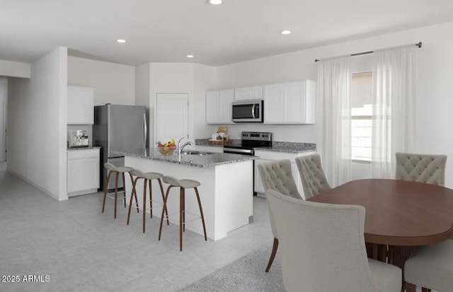 kitchen with white cabinets, light stone counters, an island with sink, and appliances with stainless steel finishes