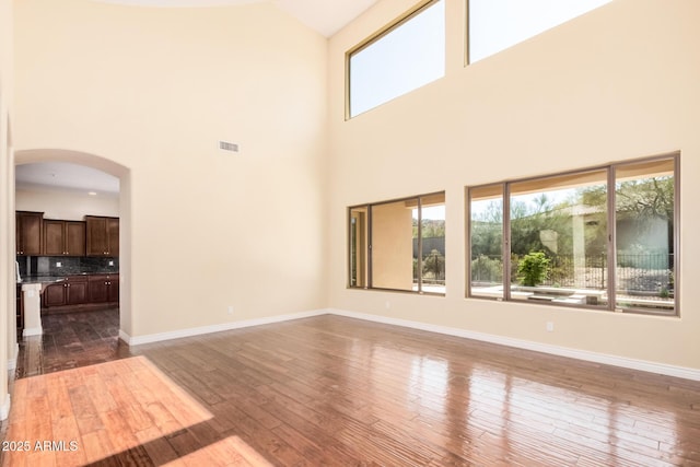 26796 N 86th Ln, Peoria, AZ 85383 - unfurnished living room with visible vents, baseboards, a towering ceiling, arched walkways, and wood-type flooring