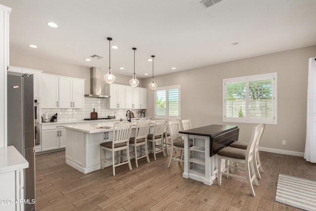 5314 N 182nd Ln, Litchfield Park, AZ 85340 - kitchen featuring wall chimney range hood, stainless steel appliances, light wood finished floors, white cabinetry, and recessed lighting