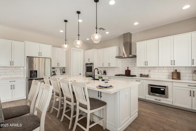 5314 N 182nd Ln, Litchfield Park, AZ 85340 - kitchen with wall chimney exhaust hood, appliances with stainless steel finishes, tasteful backsplash, white cabinets, and a center island with sink