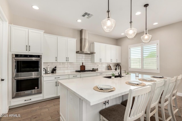5314 N 182nd Ln, Litchfield Park, AZ 85340 - kitchen featuring stainless steel double oven, wall chimney exhaust hood, light wood-style flooring, decorative backsplash, and light countertops