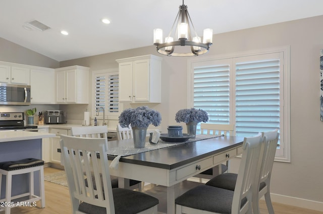 dining space featuring a notable chandelier, light hardwood / wood-style flooring, sink, and vaulted ceiling