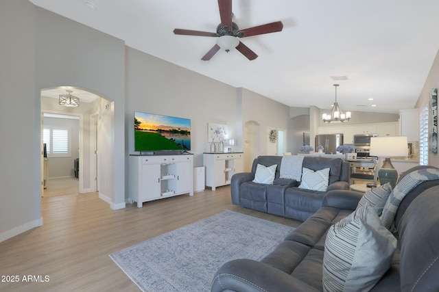 living room with ceiling fan with notable chandelier, vaulted ceiling, and light wood-type flooring