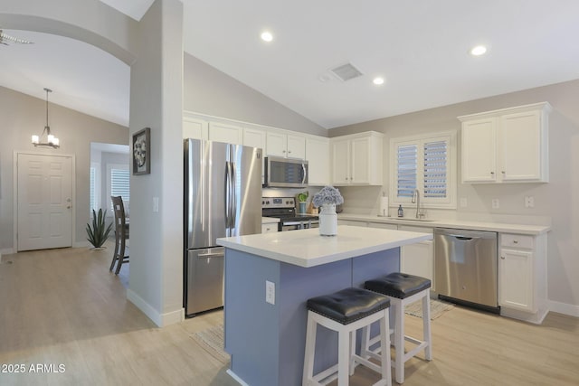 kitchen with lofted ceiling, light hardwood / wood-style flooring, white cabinetry, stainless steel appliances, and a kitchen island