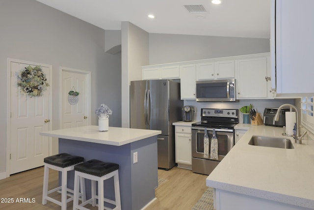 kitchen with lofted ceiling, sink, appliances with stainless steel finishes, white cabinetry, and a kitchen island