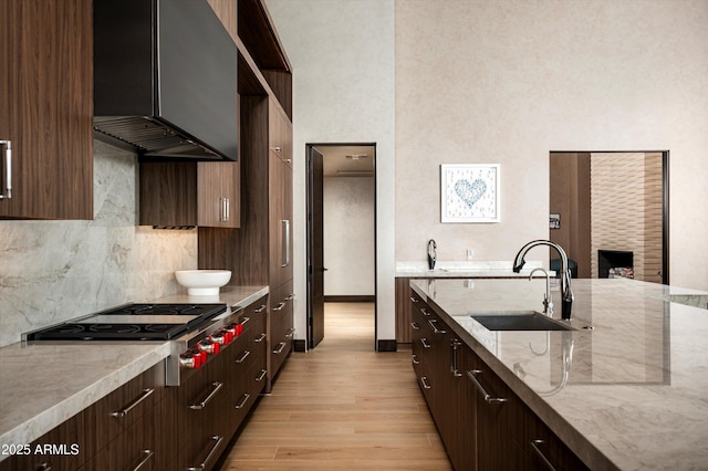 9643 E Cintarosa Pass, Scottsdale, AZ 85262 - kitchen with exhaust hood, light wood-type flooring, stainless steel gas stovetop, a sink, and backsplash