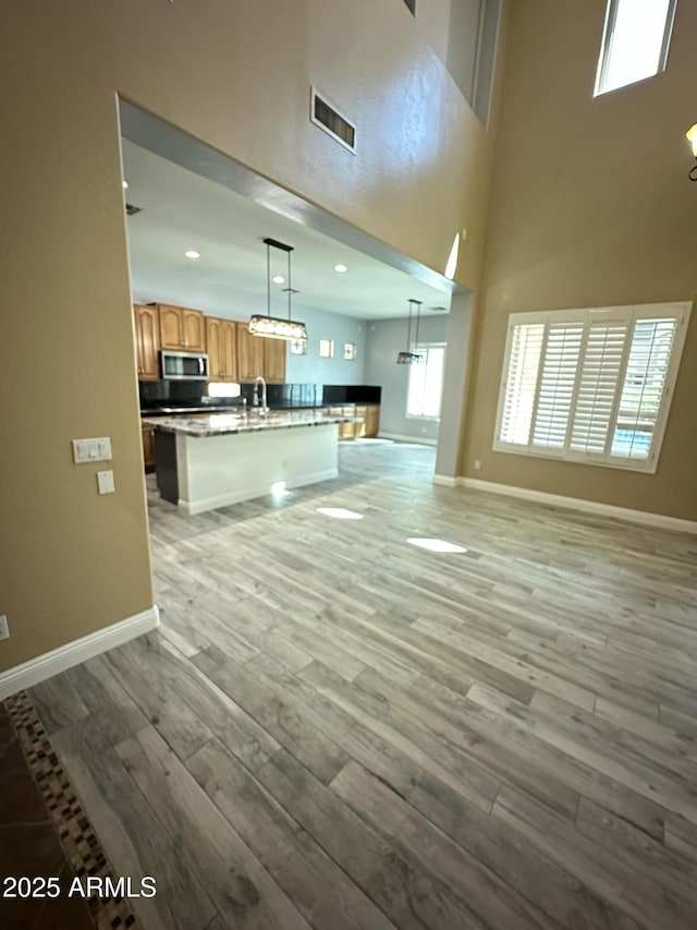 13259 W Flower St, Litchfield Park, AZ 85340 - unfurnished living room featuring baseboards, visible vents, light wood-type flooring, and a high ceiling