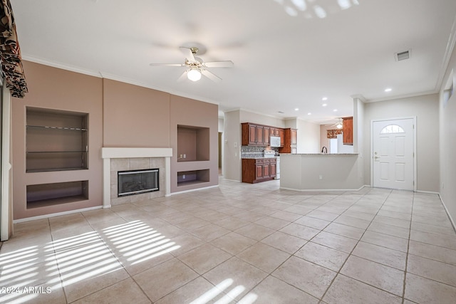 unfurnished living room featuring crown molding, built in shelves, ceiling fan, a fireplace, and light tile patterned flooring