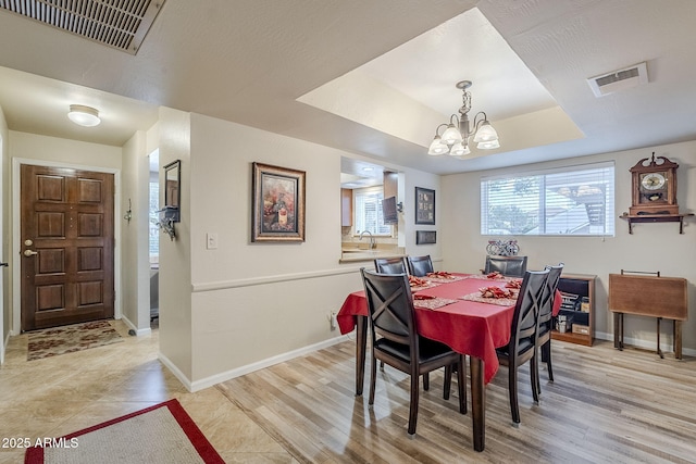 dining room featuring a chandelier, a raised ceiling, and light wood-type flooring