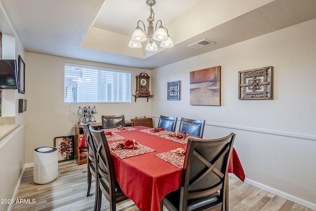 dining space featuring an inviting chandelier, a tray ceiling, and light wood-type flooring